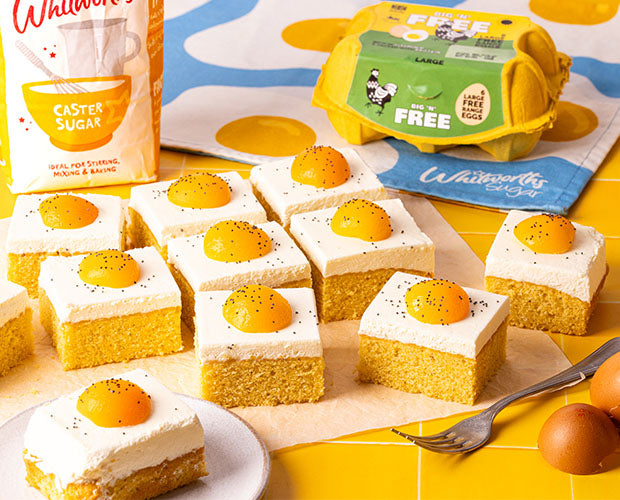 A traybake cake with a cream topping, finished with an apricot and poppy seeds to create the illusion of fried eggs