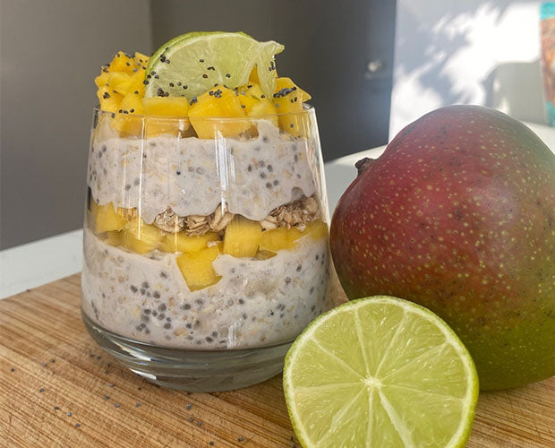 A glass filled with alternate layers of overnight oats and fresh mango, topped with a fresh lime wedge