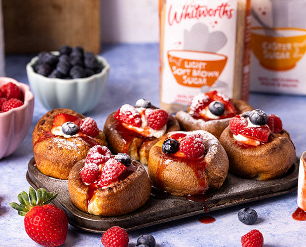 6 mini yorkshire puddings on a tray, topped with fruits and sweet strawberry syrup