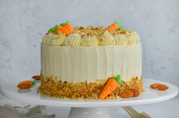 A tiered carrot cake finished with cream cheese, topped with nuts and carrot shaped icing
