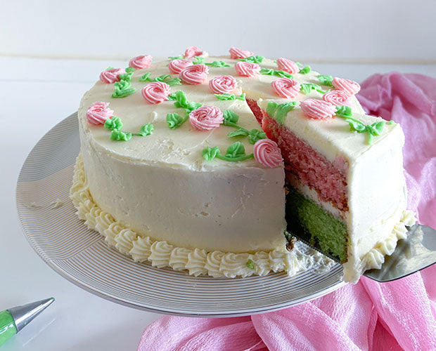 A cake with pastel pink and green layers being sliced, covered in buttercream piped with roses