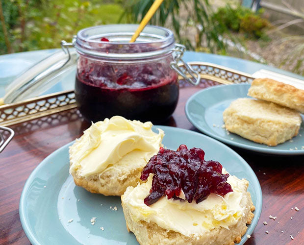 Sour cherry jam and cream on a classic scone, placed beside a fresh jar of jam.