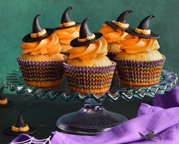 cupcakes iced with orange buttercream topped with fondant witches hats