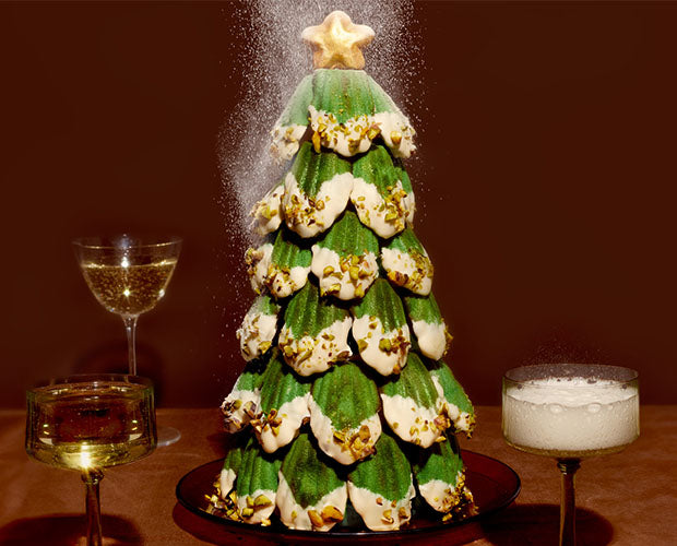 Christmas tree made from green pistachio madeleines. Dipped in white chocolate to resemble snowfall and sprinkles with crushed pistachios.