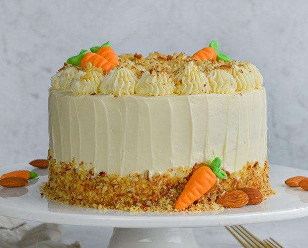 A tiered carrot cake finished with cream cheese, topped with nuts and carrot shaped icing