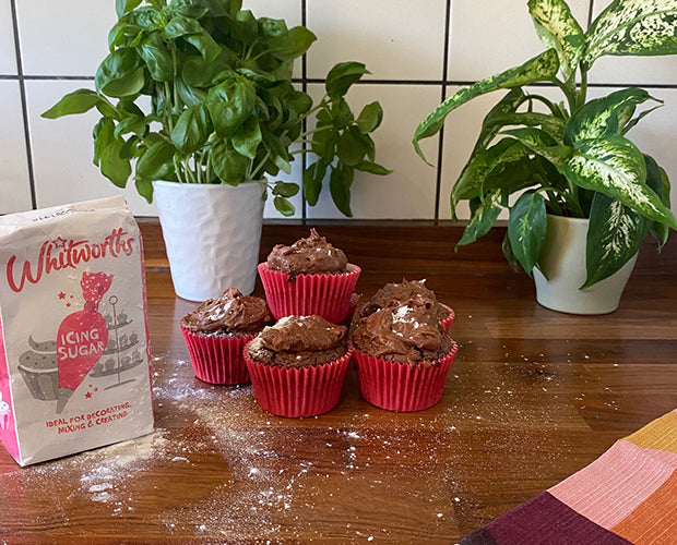 a bag of icing sugar next to a pile of chocolate and peanut butter cupcakes
