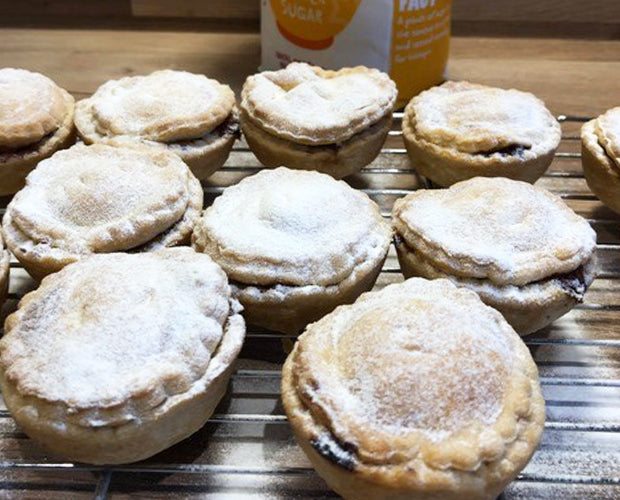 Mince pies sprinkled with icing sugar drying on a tray