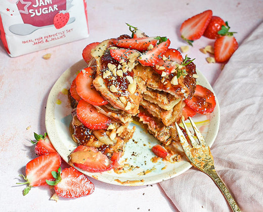 A plate loaded with pancakes, fruits, and jam 