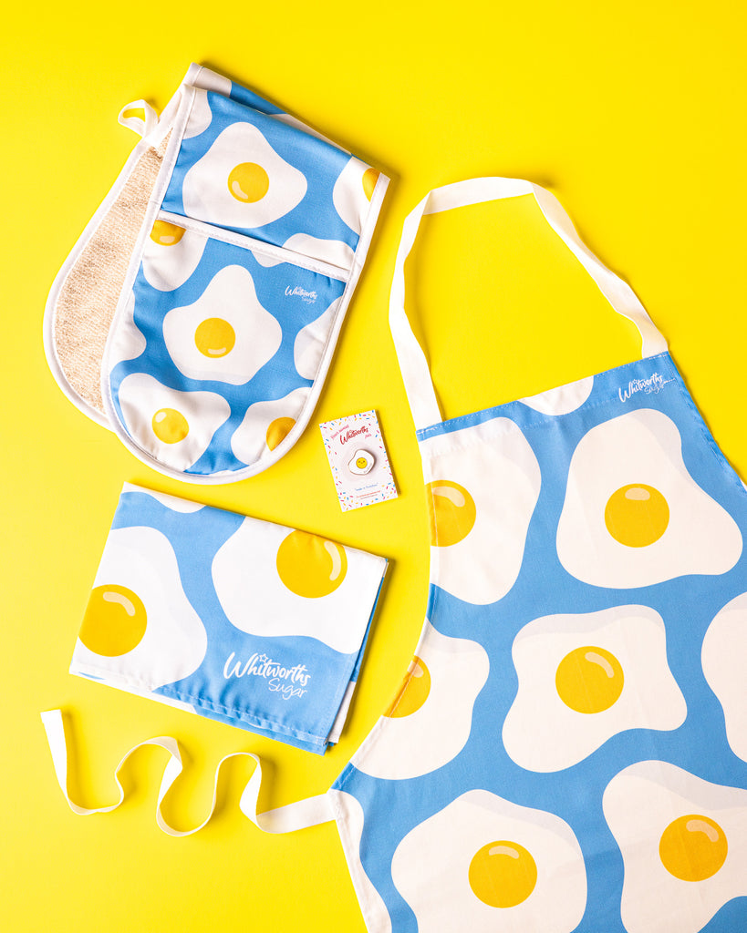 Flat lay of Blue Sunny Egg bundle including tea towel, oven glove, apron and pin